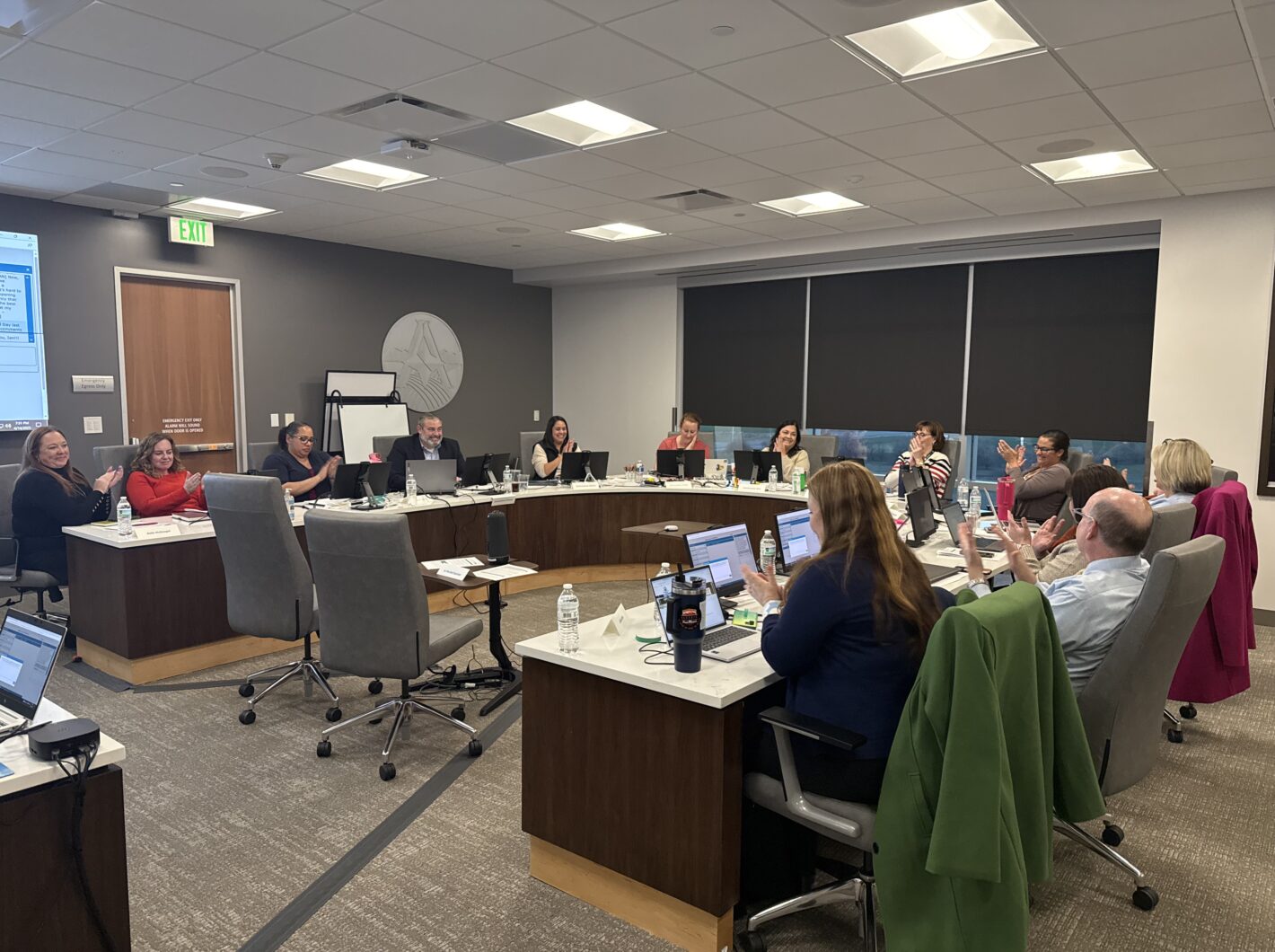 People in a conference room smiling and clapping at a meeting.