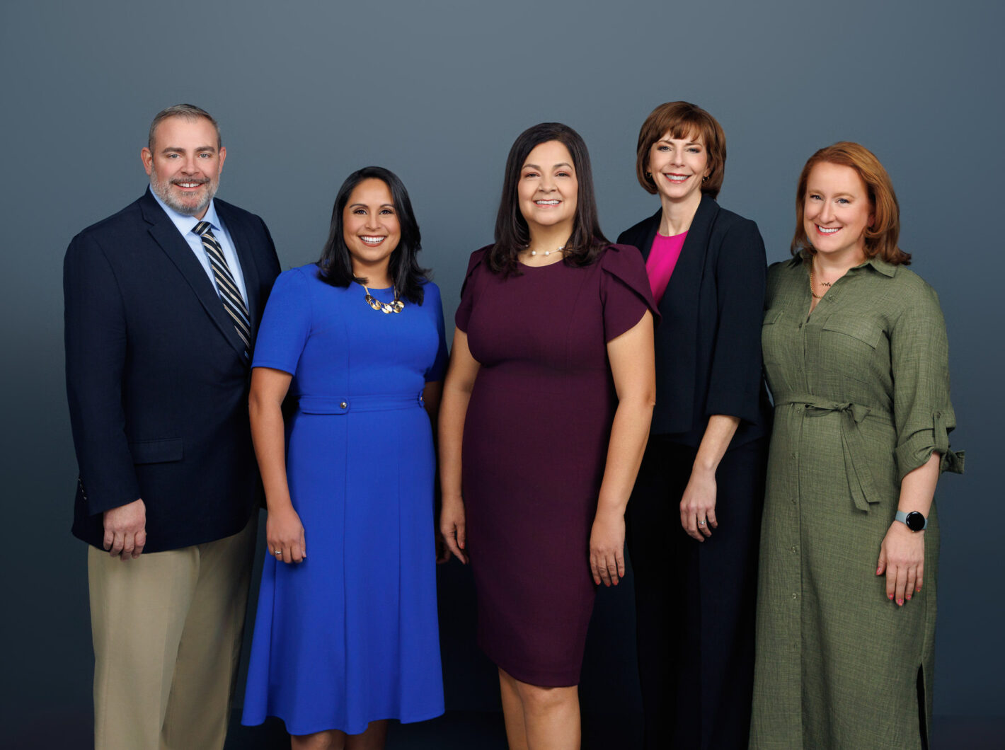 Adams-Cty-0379-WEB.jpg shows five individuals standing in front of a gray background, smiling and wearing business attire.