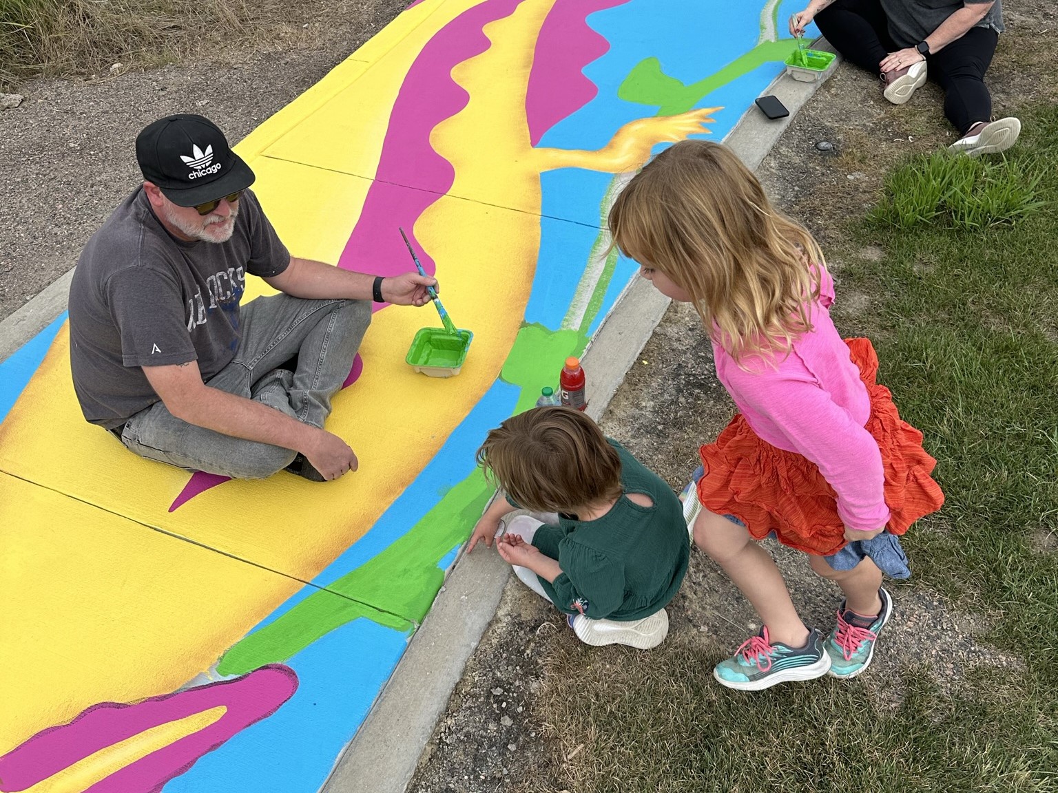 Man and children painting colorful sidewalk mural, creating community art.