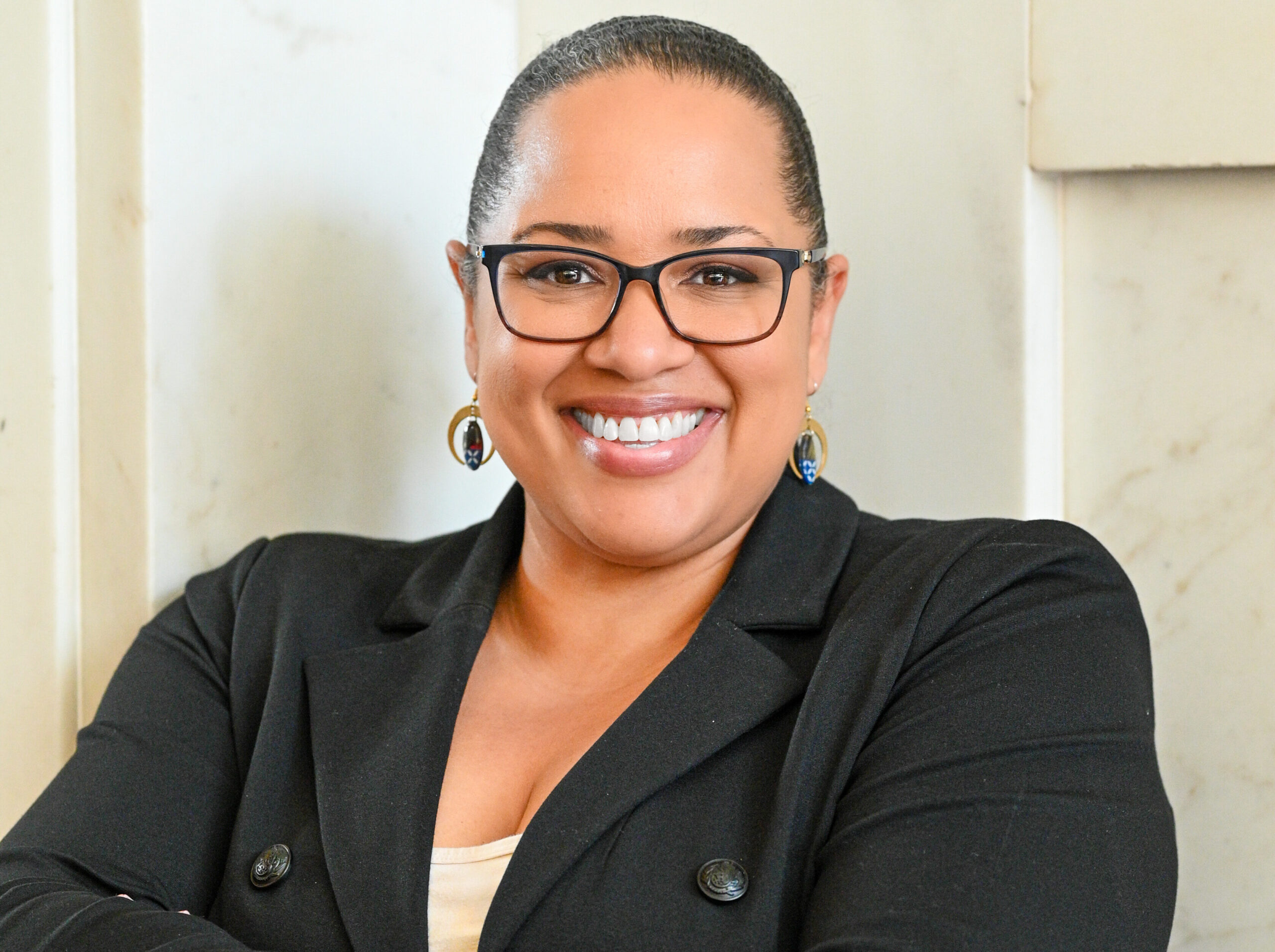 Dionne Stroter smiling confidently, wearing glasses and a black blazer.