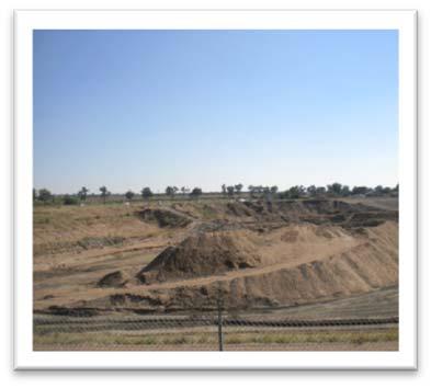 Expansive industrial site with mounds of excavated earth under a clear blue sky.