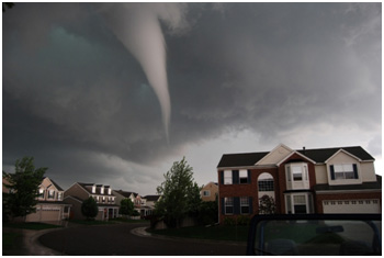 Tornado funnel cloud looming over suburban neighborhood under dark, stormy skies.
