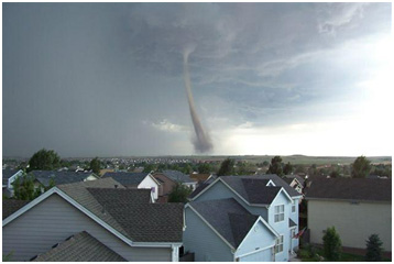 Tornado funnel approaching residential neighborhood under dark, stormy sky.