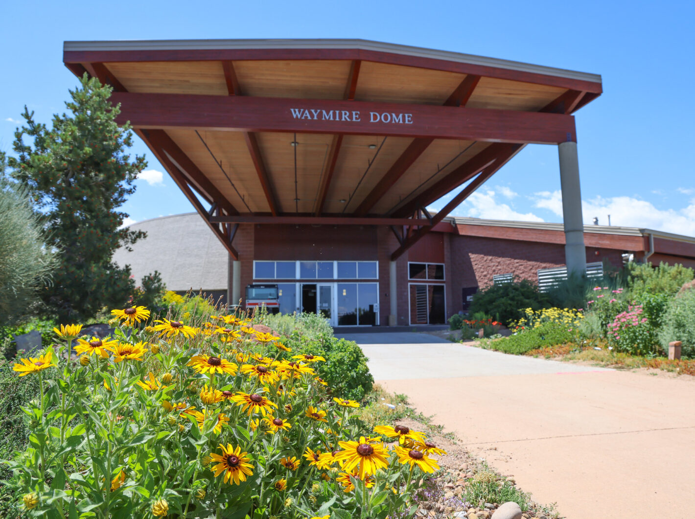 Waymire Dome entrance with gardens, featuring yellow flowers and greenery on a sunny day