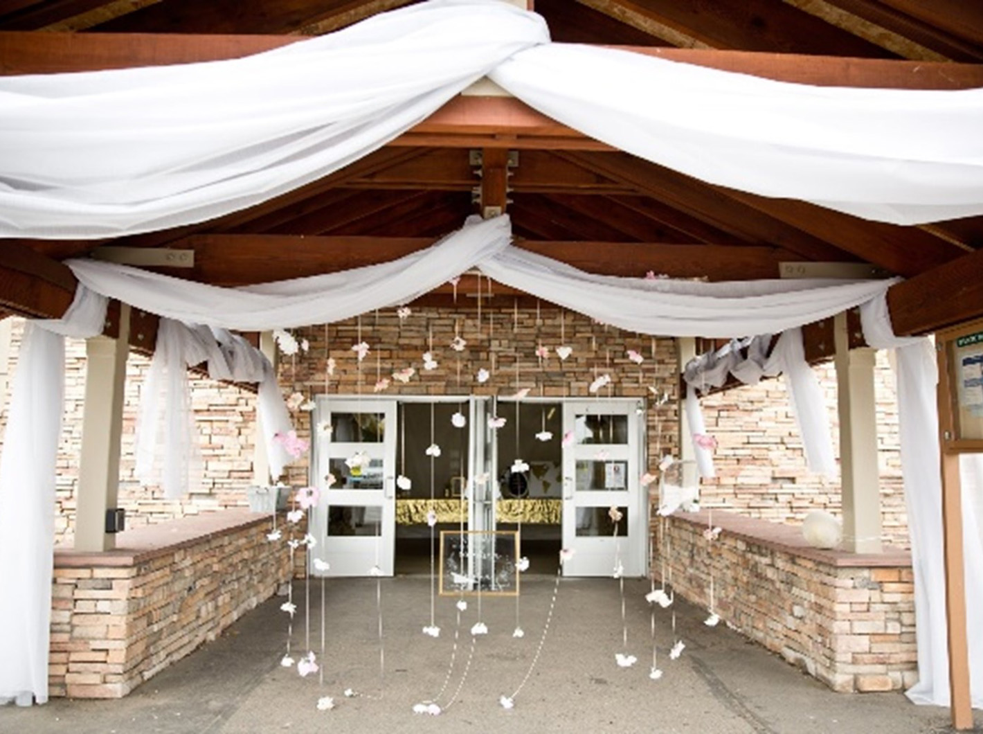 Wooden entrance adorned with white drapery and hanging flowers, leading to double doors.
