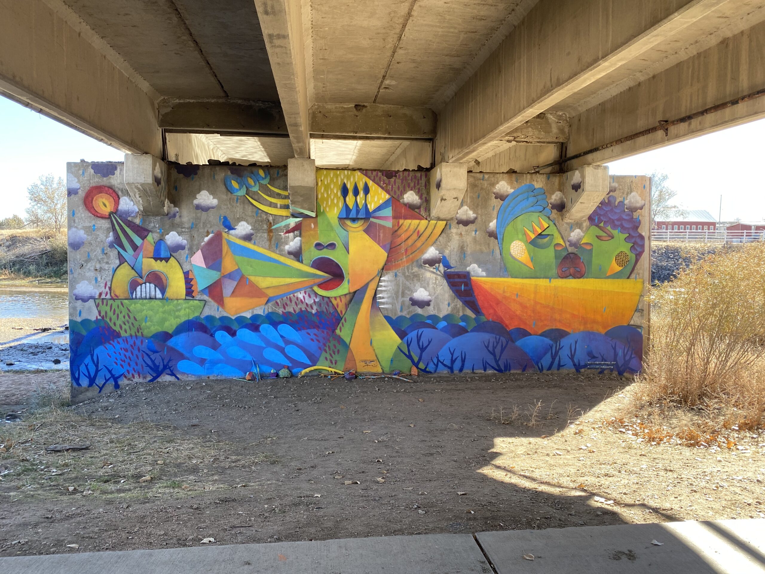 Colorful mural of abstract faces and shapes under a bridge.