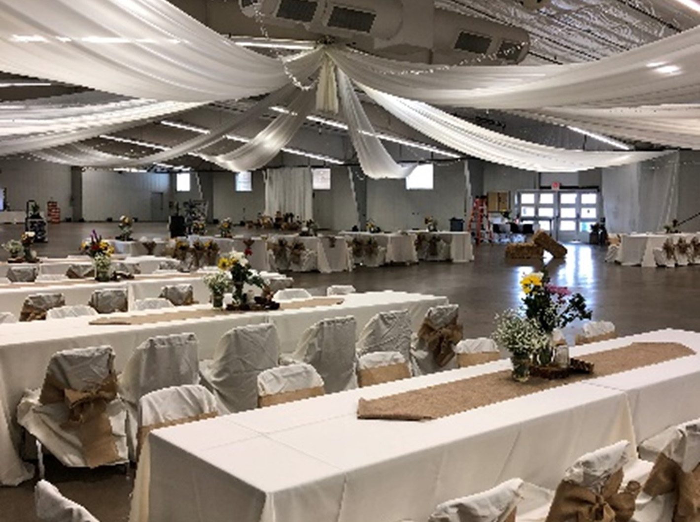 Banquet hall with white drapes, decorated tables, and floral centerpieces.