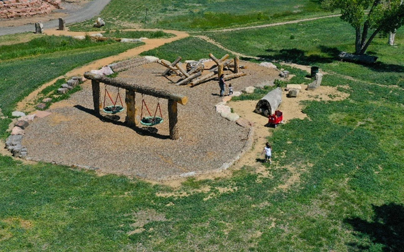 Playground with wooden swings and climbing structures, surrounded by grassy paths and children playing.