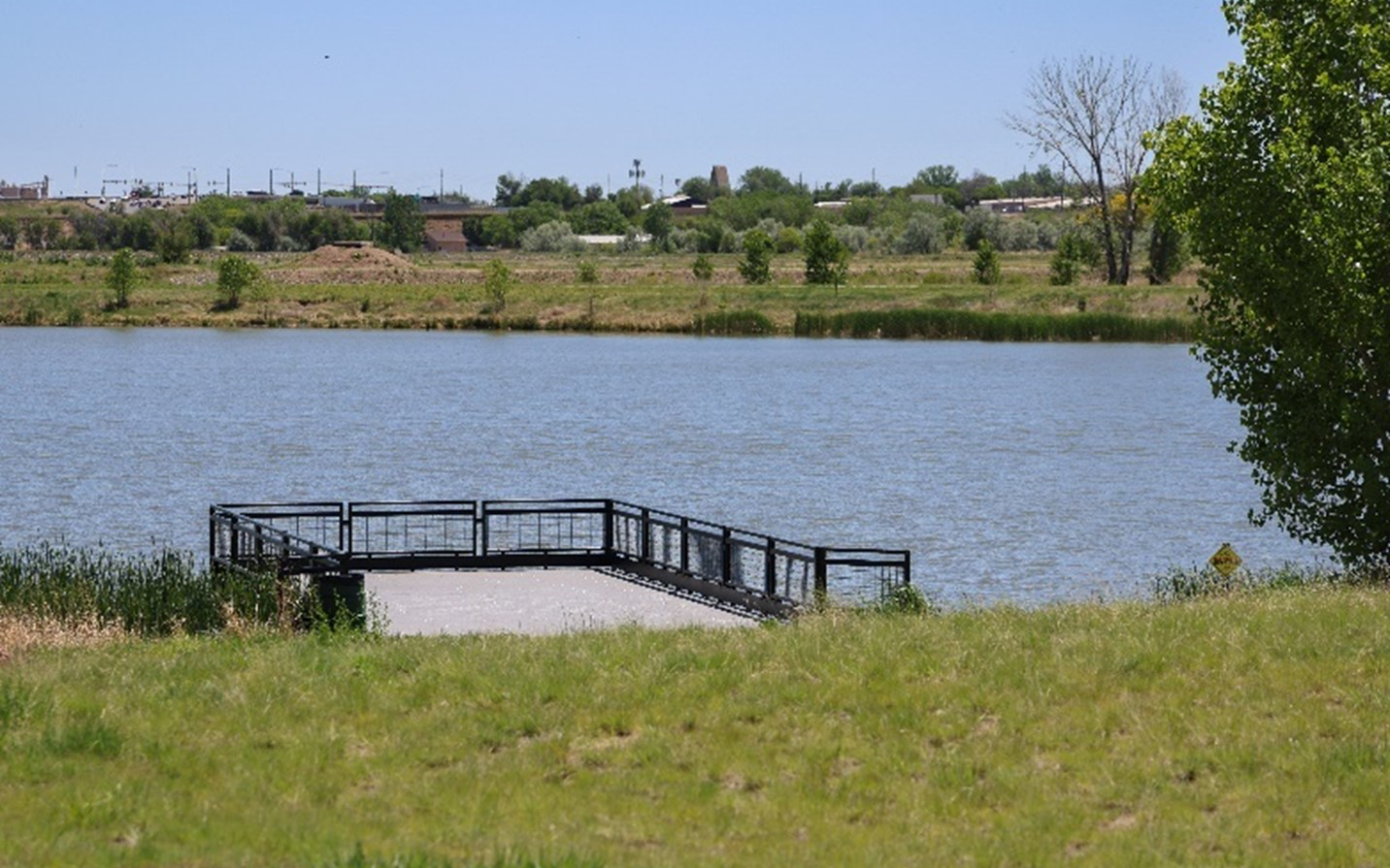 Viewing platform overlooking a calm lake, surrounded by green fields and distant trees.