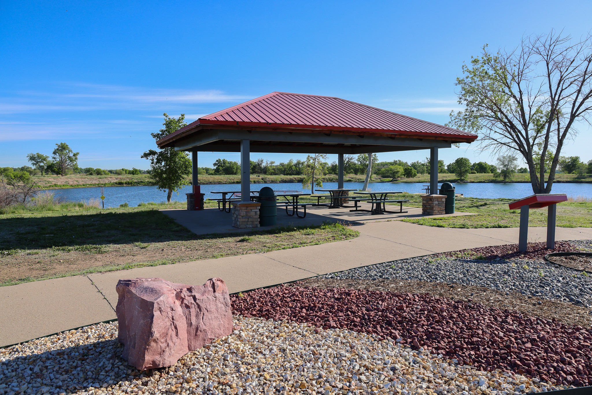 Pavilion with metal roof, picnic tables, and view of a lake.