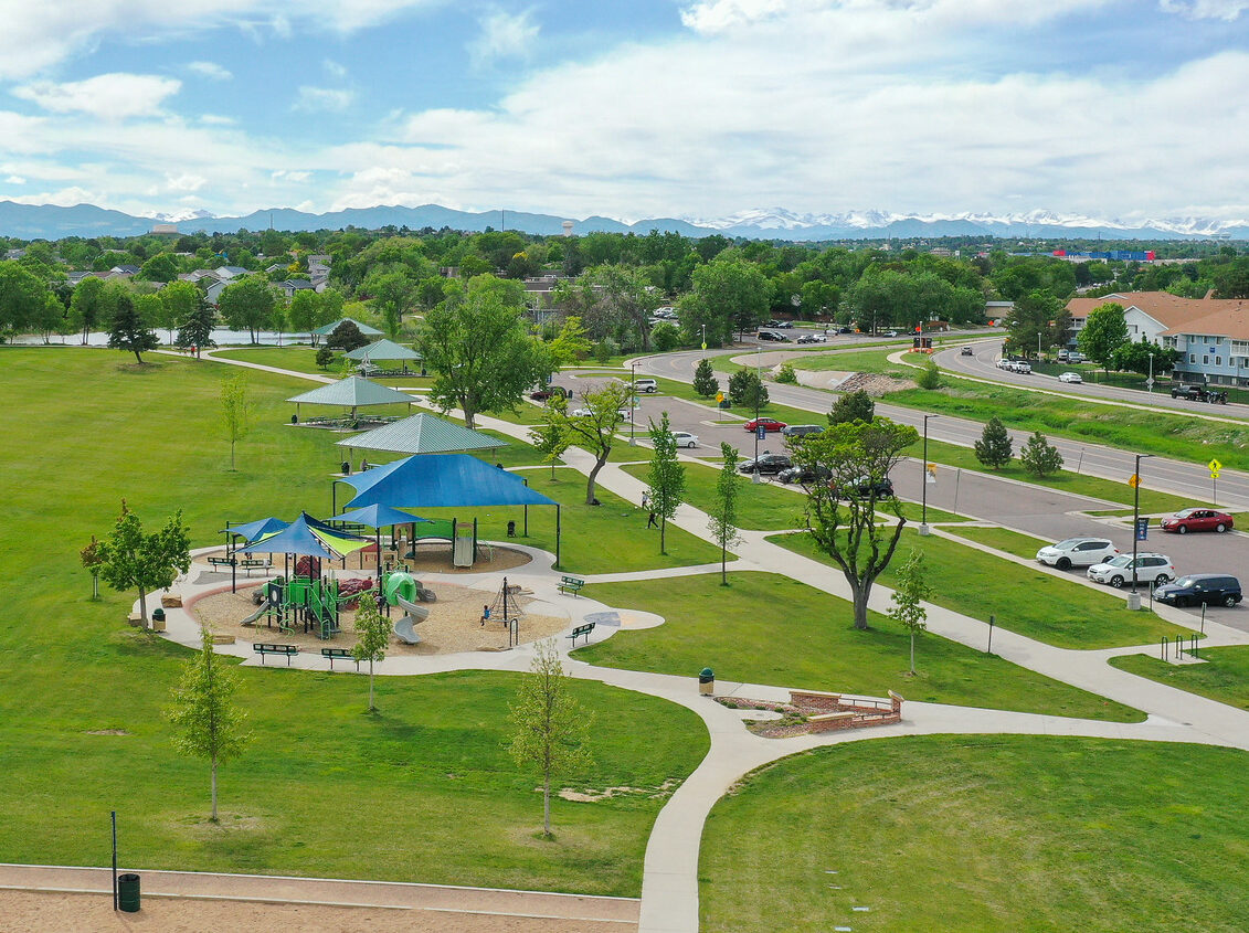 Aerial view of a large park with green fields, a blue-roofed playground, pathways, and a distant mountain range.