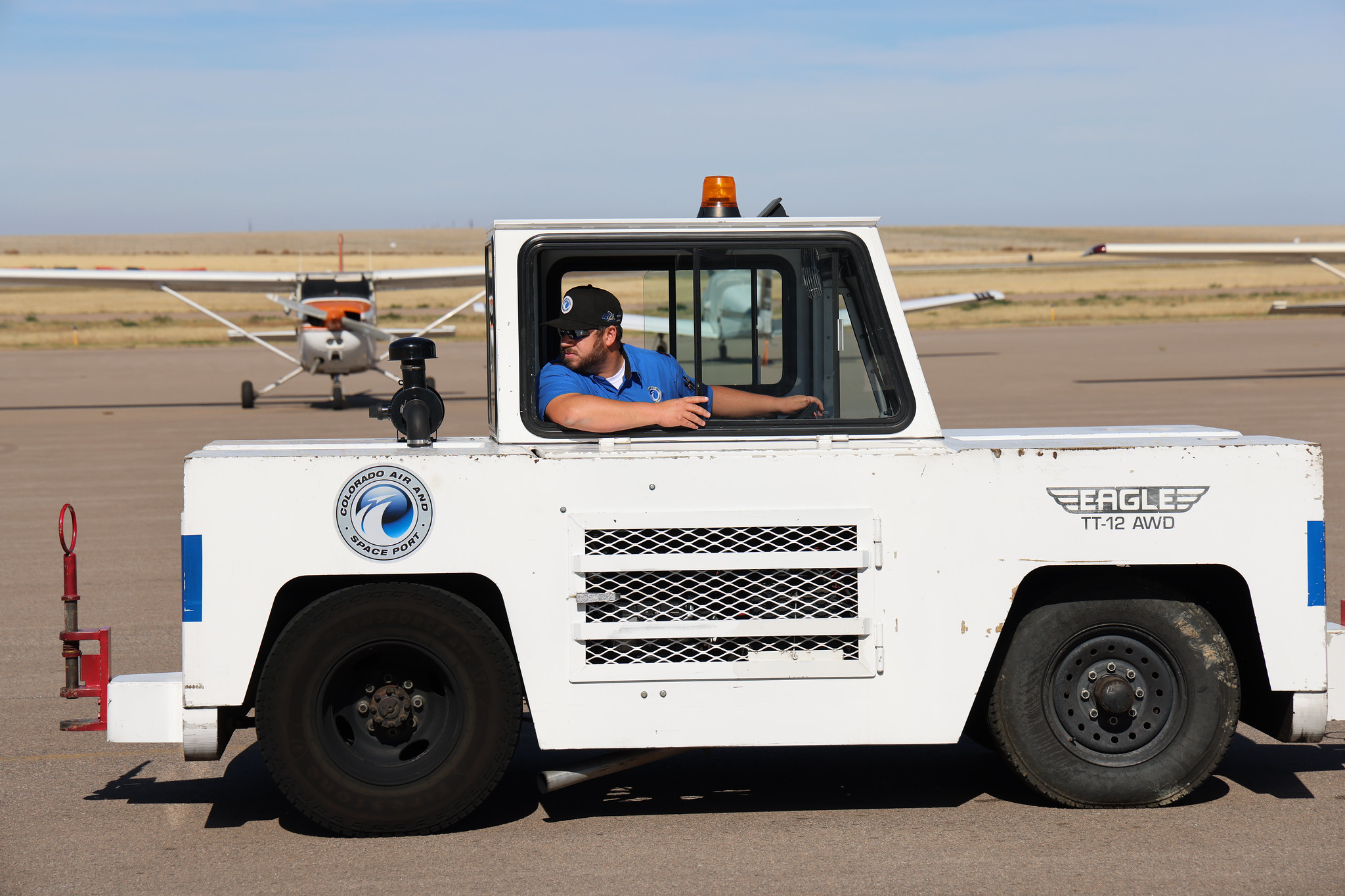 Man in vehicle at airport, Colorado Air and Space Port logo, plane in background