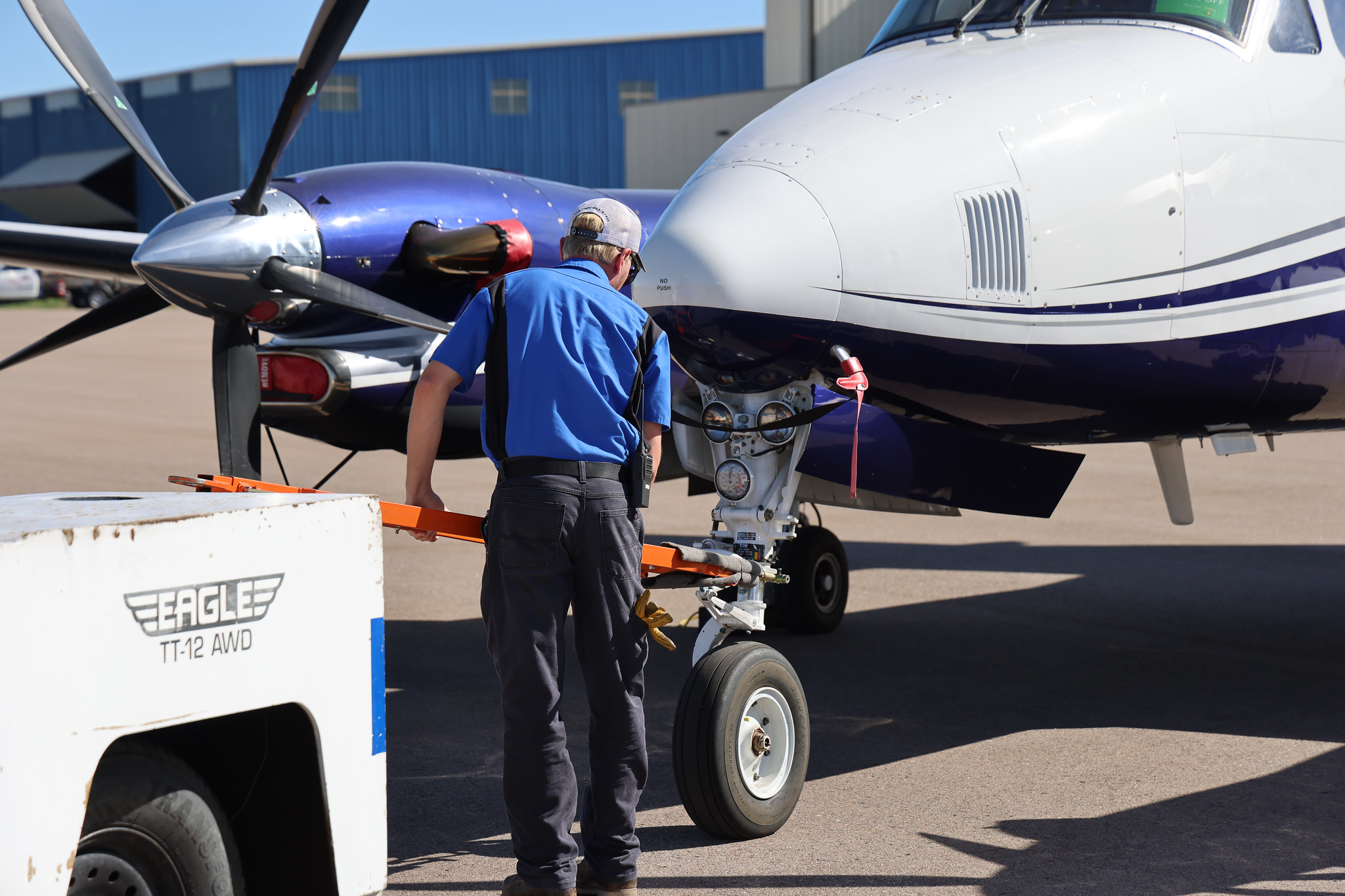 Person in blue shirt maneuvering a small aircraft with a tow bar.