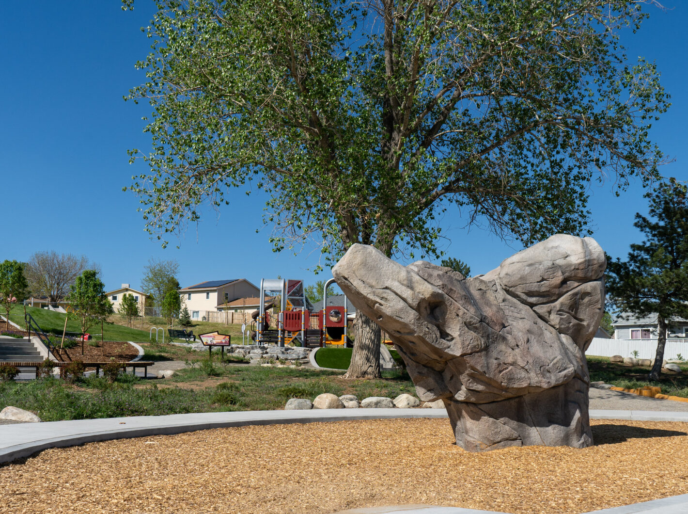 Playground with climbing rock in park, large tree, clear sky