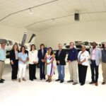 Group of 13 people posing in front of two small airplanes in a hangar