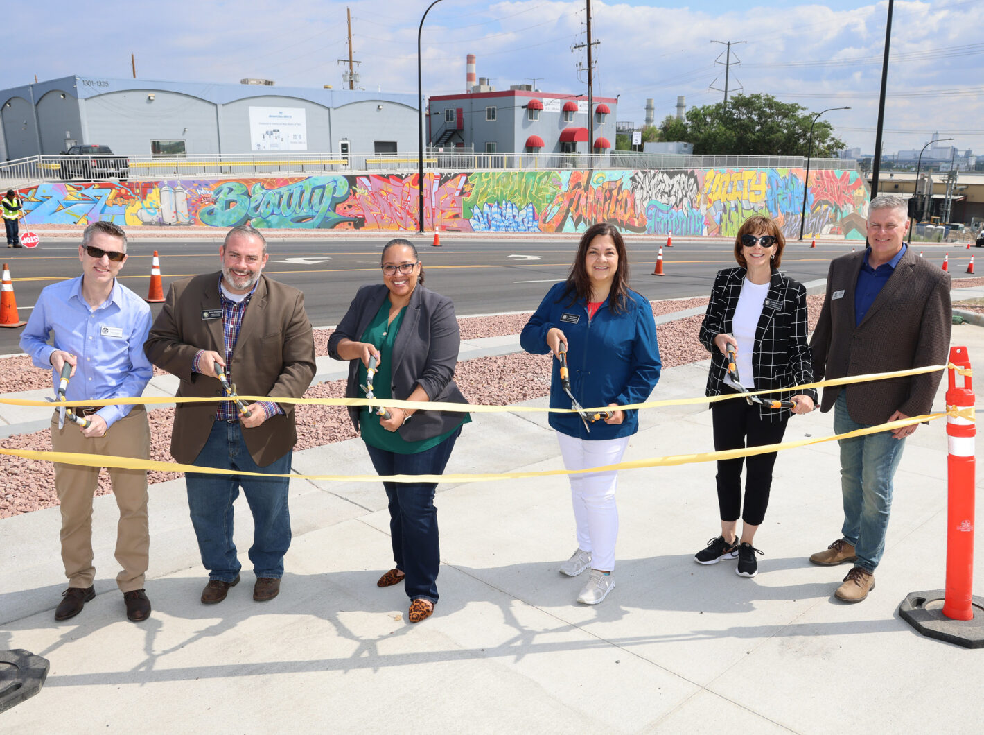 This photo showcases six people cutting a ribbon at a ceremony with a colorful mural in the background