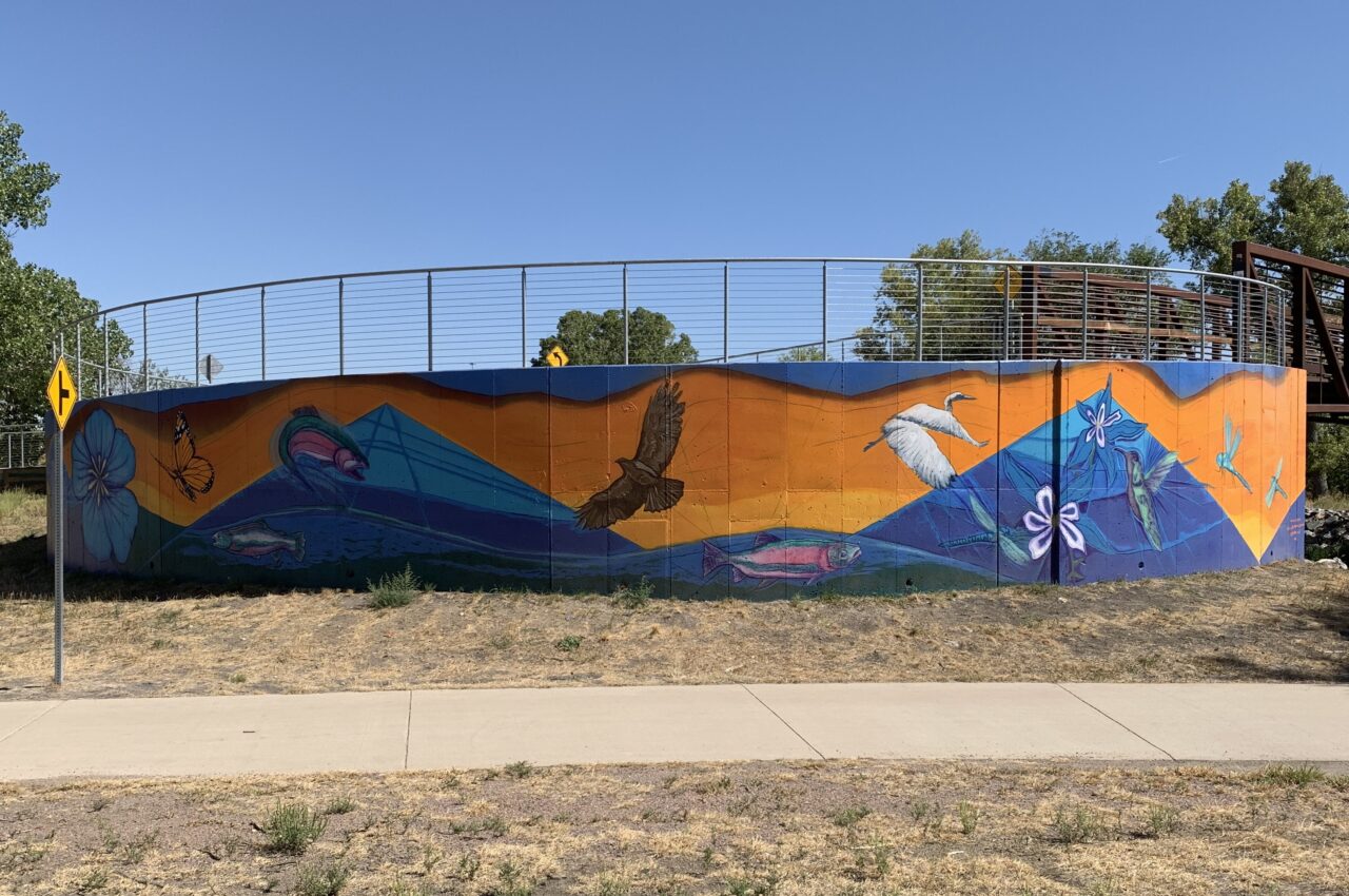 Colorful mural on a curved wall featuring birds, fish, and flowers against a vibrant orange and blue backdrop.