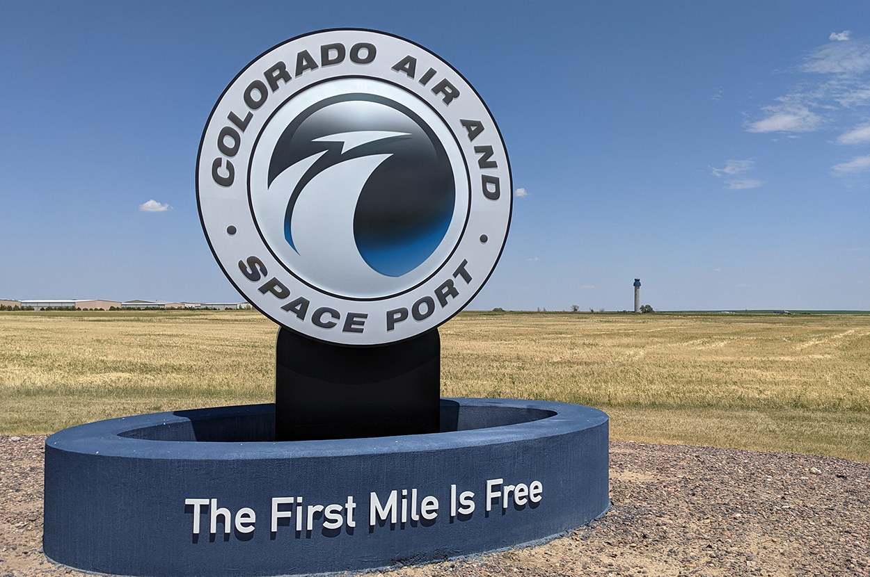 Colorado Air and Space Port sign with slogan "The First Mile Is Free" against clear sky and open field.