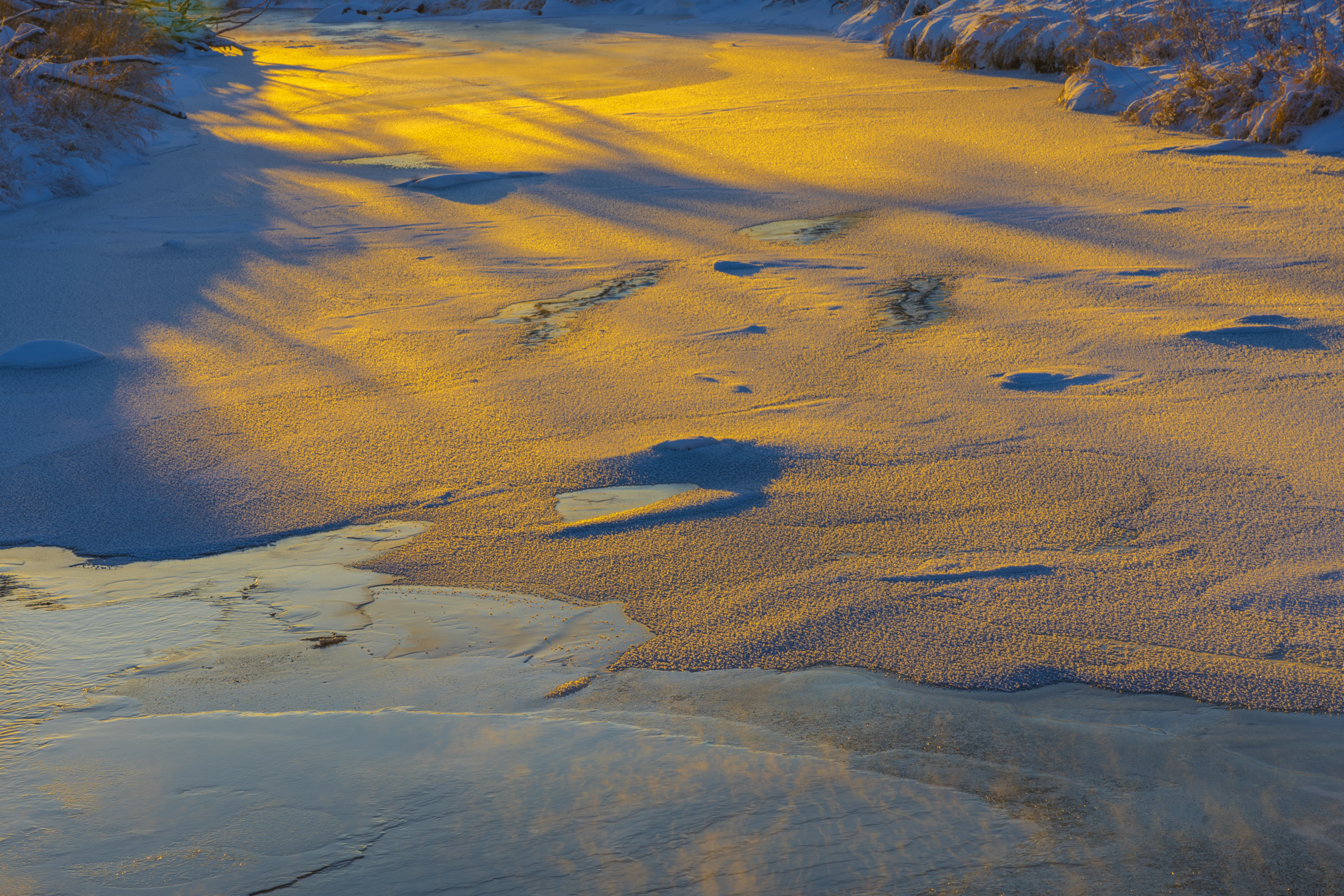Golden sunrise light on a snowy, frozen creek in winter.