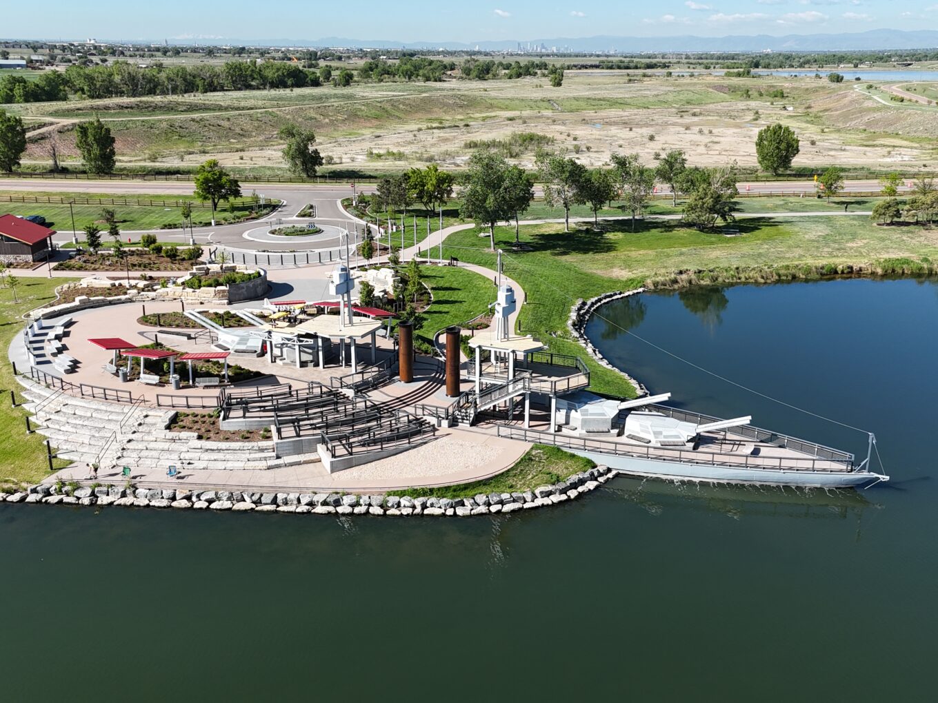Aerial view of an amphitheater by a lake, surrounded by greenery and pathways.