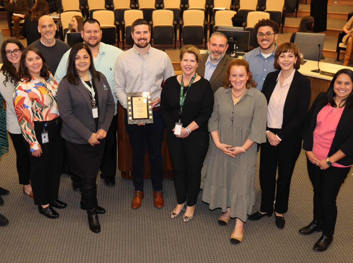Group of people smiling, one holding an award plaque, in a formal setting