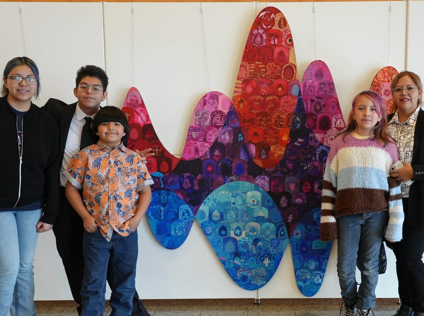 Five people smiling in front of colorful abstract wall art, expressing happiness and togetherness
