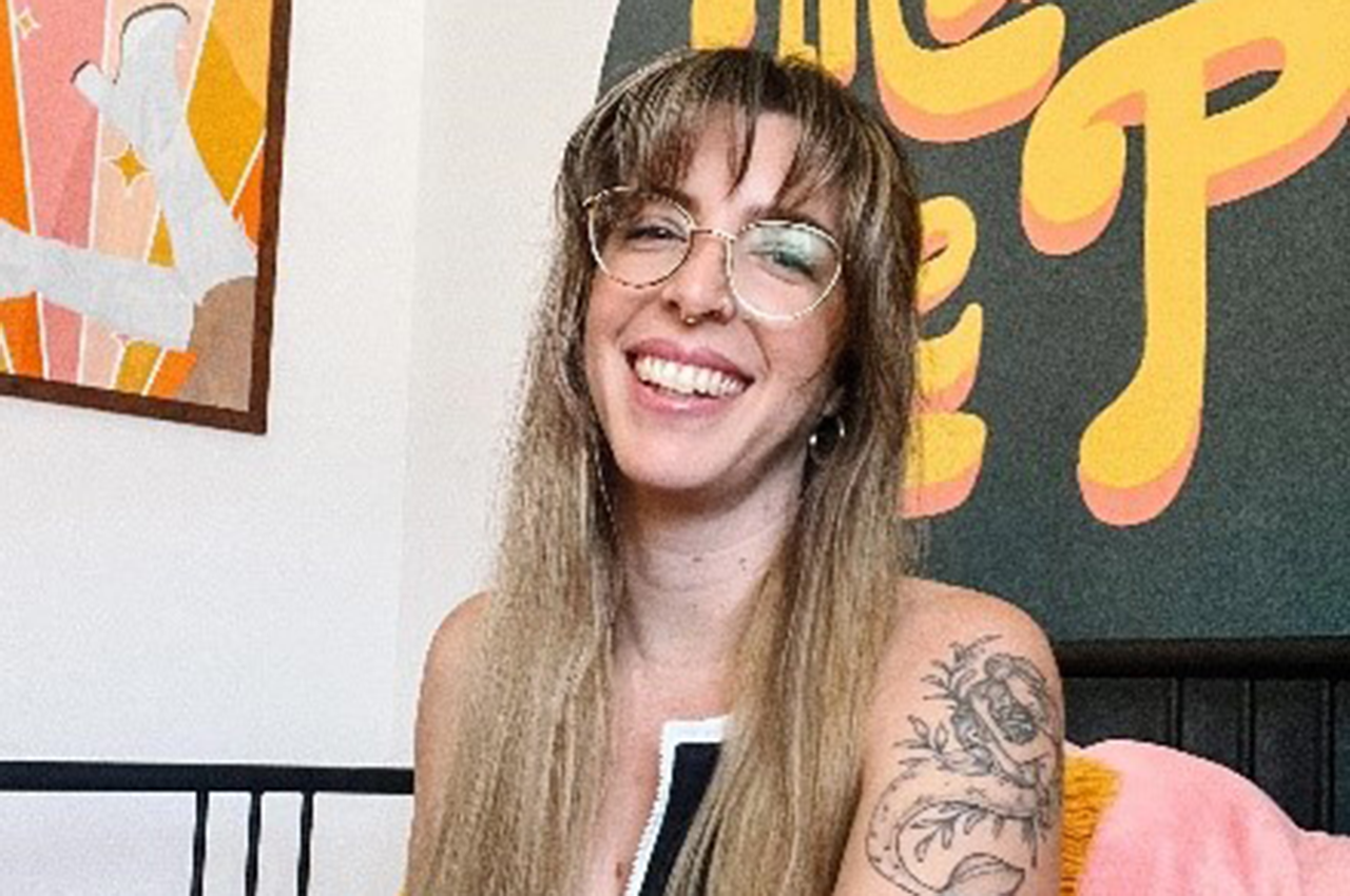 Marina smiling with long hair, round glasses, and a floral tattoo on her arm.