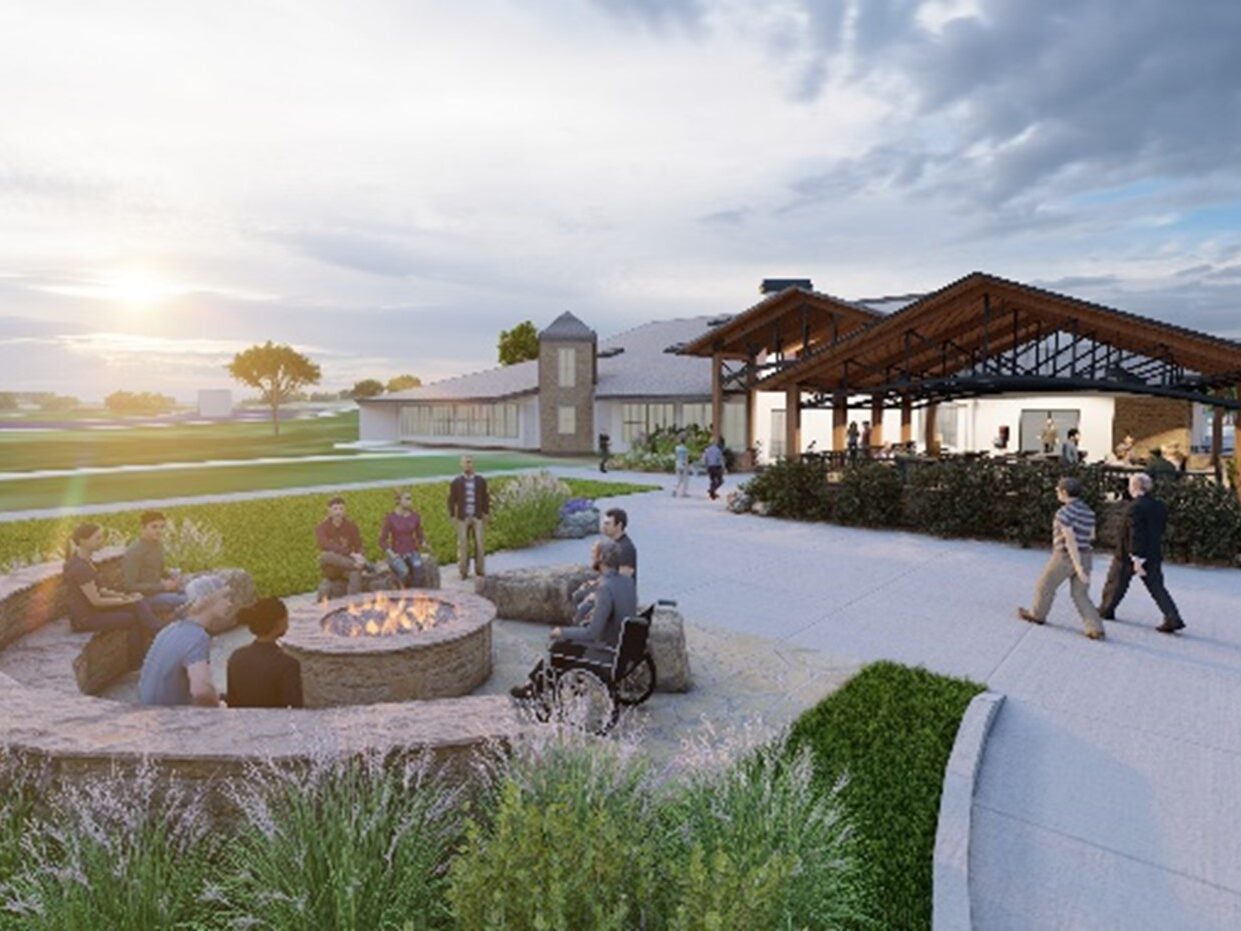 People gather around a fire pit near a modern building at sunset.