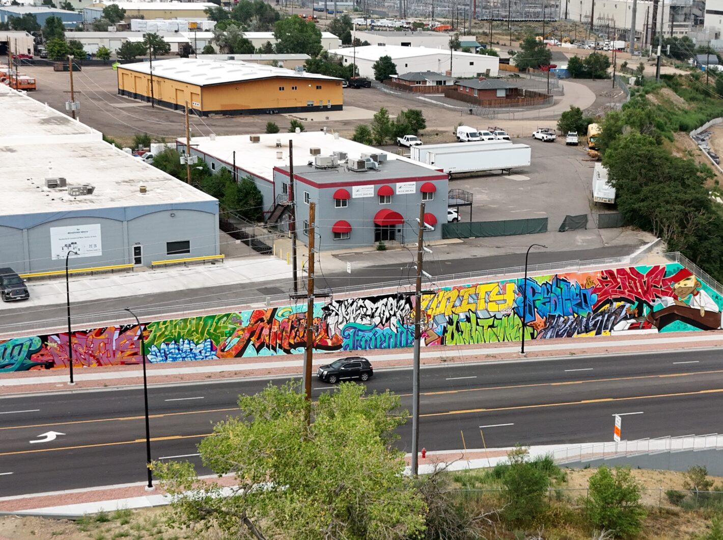 Colorful graffiti mural on a long urban wall next to industrial buildings