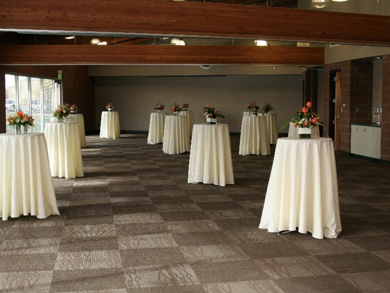 Rendezvous room setup with round cocktail tables, white tablecloths, and orange floral arrangements.