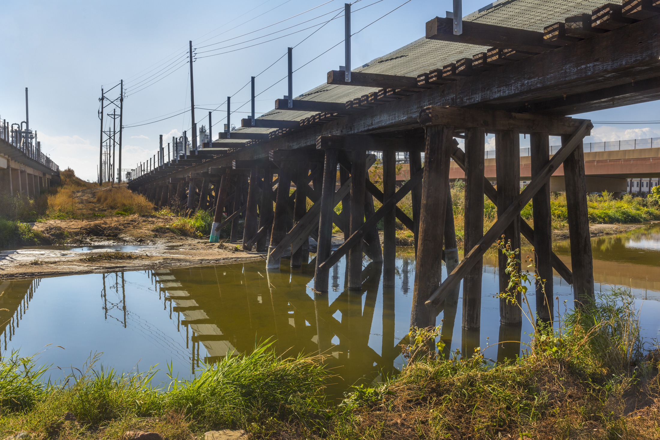 Wooden bridge spans over a calm river, reflecting the structure and sky.