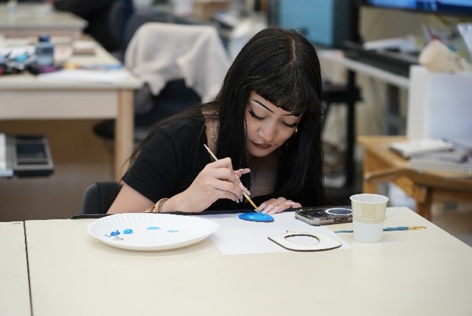 Student painting with blue on a small canvas, focused and engaged
