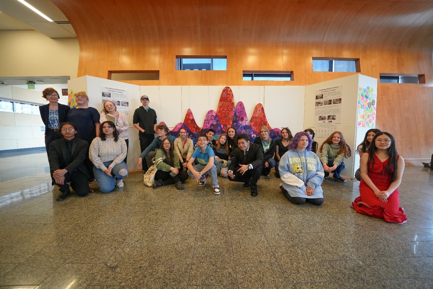 Unveiling-Group-Photo.jpg: Diverse group of people smiling in front of colorful art installation indoors.